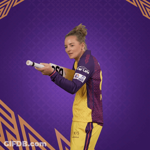 A Woman In A Yellow And Purple Jersey Holding A Dsc Bat GIF