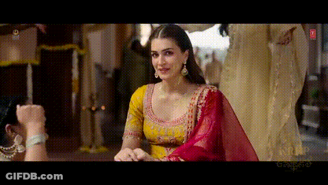 A Woman In A Yellow And Red Dress Is Standing In Front Of A Man . GIF