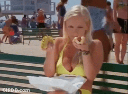 A Woman In A Yellow Bikini Is Sitting On A Bench Eating A Donut GIF