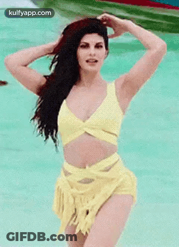 A Woman In A Yellow Bikini Is Standing In A Pool Of Water . GIF