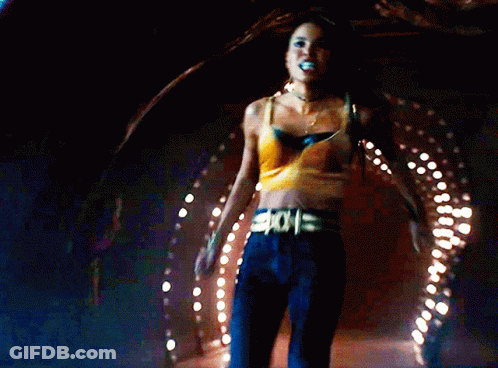 A Woman In A Yellow Crop Top Is Holding Another Woman In A Dark Room GIF