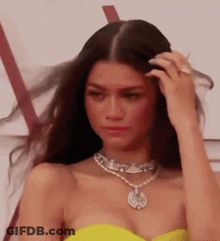 A Woman In A Yellow Dress And Necklace Is Touching Her Hair . GIF