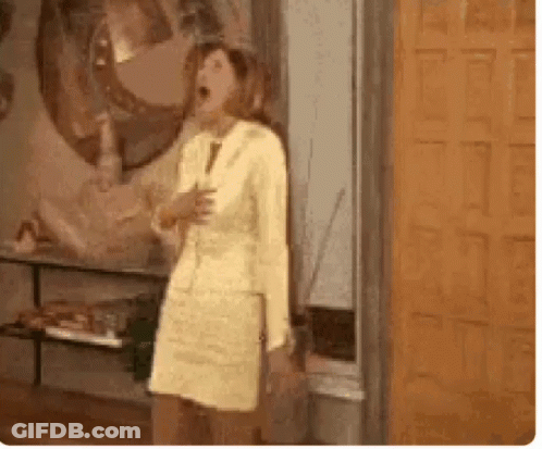 A Woman In A Yellow Dress And Suit Is Standing In Front Of A Door . GIF