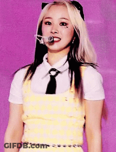 A Woman In A Yellow Dress And Tie Is Standing In Front Of A Microphone . GIF