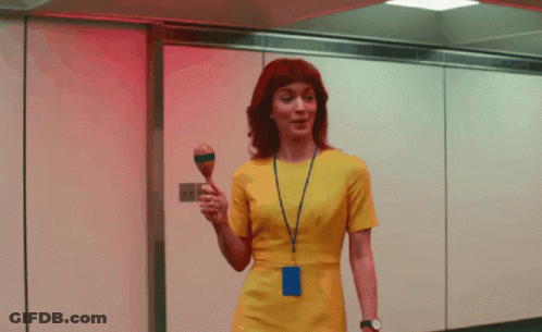 A Woman In A Yellow Dress Is Holding A Maraca In Her Hand GIF