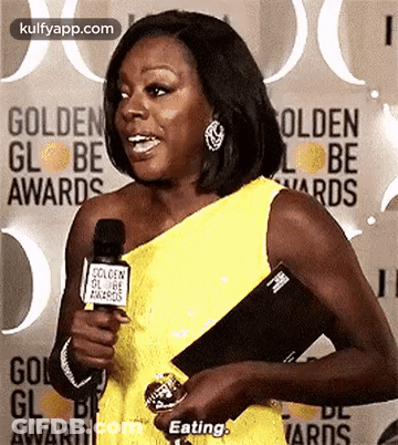 A Woman In A Yellow Dress Is Holding A Microphone And Talking Into It At The Golden Globe Awards . GIF