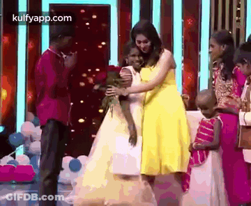 A Woman In A Yellow Dress Is Hugging A Little Girl In A White Dress On A Stage . GIF