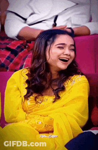 A Woman In A Yellow Dress Is Laughing With Her Eyes Closed GIF