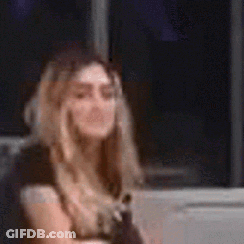 A Woman In A Yellow Dress Is Sitting In Front Of A Window And Talking On A Cell Phone . GIF