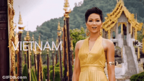 A Woman In A Yellow Dress Is Standing In Front Of A Row Of Gold Buildings And The Word Vietnam Is On The Bottom GIF