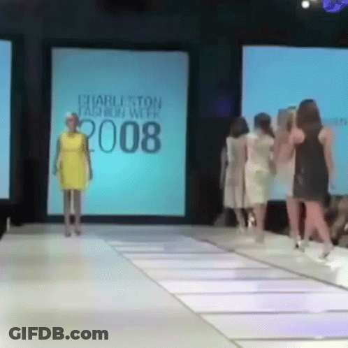 A Woman In A Yellow Dress Is Walking Down A Runway At The Charleston Fashion Week 2008 GIF