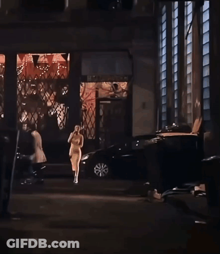 A Woman In A Yellow Dress Is Walking Down A Street In Front Of A Building With A Sign That Says Home Depot GIF