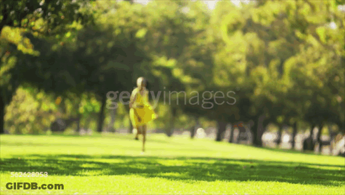 A Woman In A Yellow Dress Is Walking Through A Park GIF