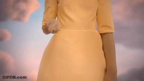 A Woman In A Yellow Dress Reaches Out Her Hand Towards A Cloudy Sky GIF