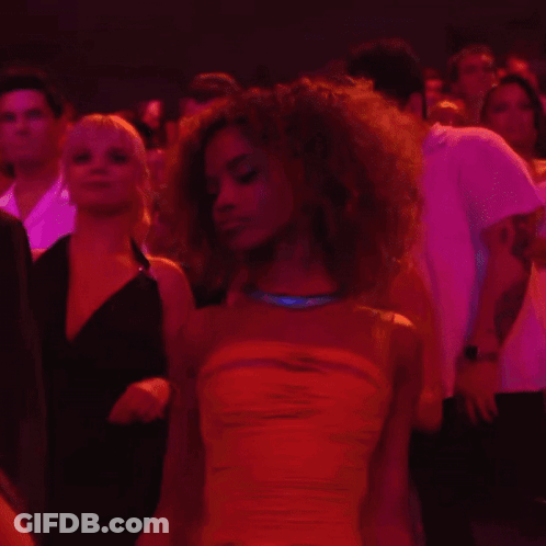 A Woman In A Yellow Dress Stands In A Crowd Of People GIF