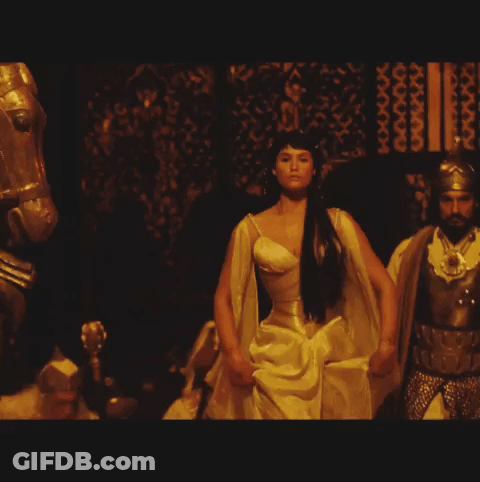 A Woman In A Yellow Dress Stands In Front Of A Man In Armor GIF