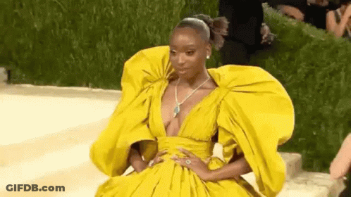 A Woman In A Yellow Dress With A Plunging Neckline And Huge Sleeves Is Sitting On The Ground . GIF