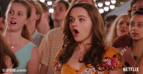 A Woman In A Yellow Floral Dress Stands In A Crowd With Her Mouth Open And A Netflix Logo In The Background GIF