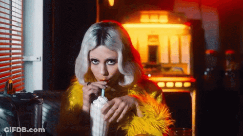 A Woman In A Yellow Fur Coat Drinking A Milkshake Through A Straw . GIF