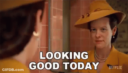A Woman In A Yellow Hat Is Looking At Her Reflection In A Mirror And Saying `` Looking Good Today '' . GIF