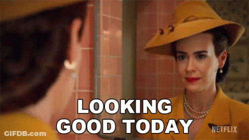 A Woman In A Yellow Hat Is Looking At Herself In A Mirror And Saying Looking Good Today . GIF