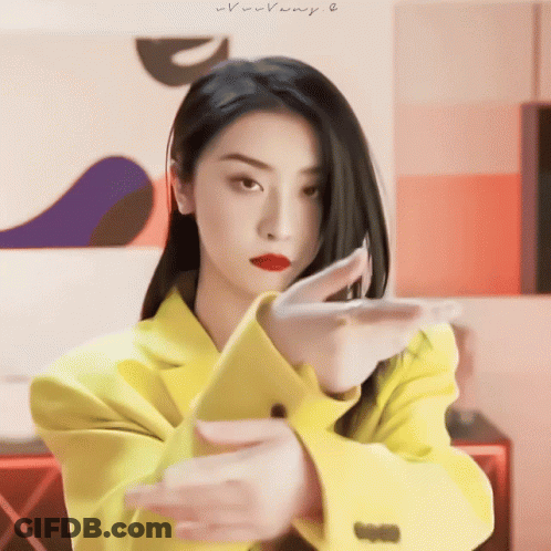 A Woman In A Yellow Jacket Is Making A Gesture With Her Arms GIF