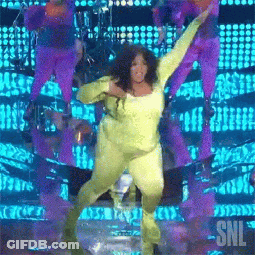 A Woman In A Yellow Jumpsuit Is Dancing On A Stage With Snl Written On The Bottom GIF