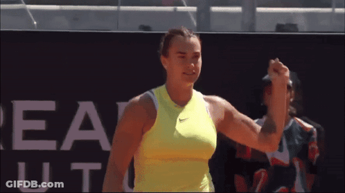 A Woman In A Yellow Nike Tank Top Holds Her Fist Up GIF