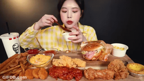 A Woman In A Yellow Plaid Shirt Is Eating A Kfc Hamburger And French Fries GIF