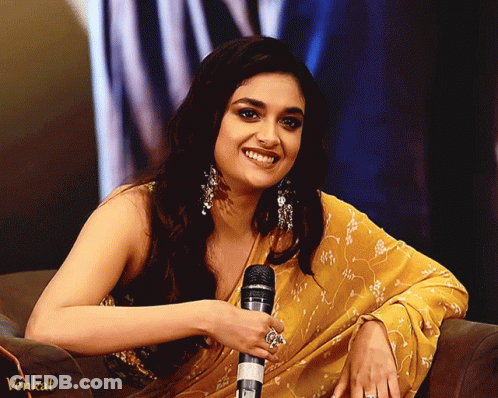 A Woman In A Yellow Saree Is Smiling While Holding A Microphone And The Word Venkat Is On The Bottom Right GIF