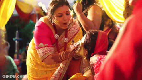 A Woman In A Yellow Sari Is Applying Powder To Another Woman 'S Face . GIF