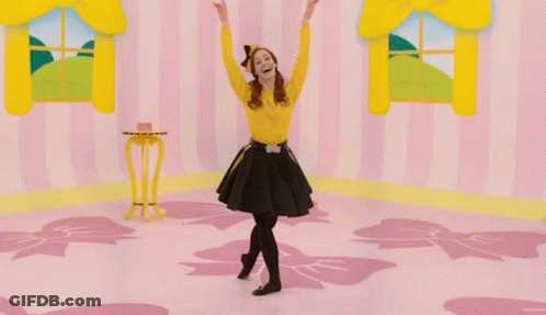A Woman In A Yellow Shirt And Black Skirt Is Dancing In A Pink Room GIF