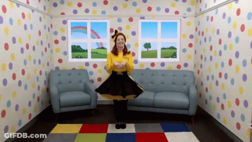 A Woman In A Yellow Shirt And Black Skirt Is Dancing In A Room With Polka Dot Wallpaper GIF