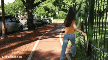 A Woman In A Yellow Shirt And Blue Jeans Is Walking Down A Bike Path GIF