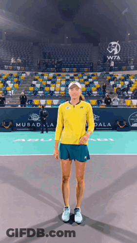 A Woman In A Yellow Shirt And Blue Shorts Is Standing On A Tennis Court GIF