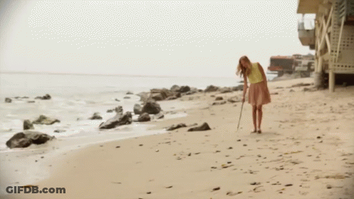 A Woman In A Yellow Shirt And Pink Skirt Is Walking Along The Beach GIF