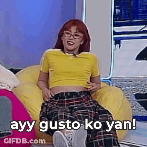 A Woman In A Yellow Shirt And Plaid Pants Is Sitting On A Bean Bag Chair With Her Legs Crossed . GIF