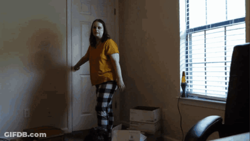 A Woman In A Yellow Shirt And Plaid Pants Is Standing In A Dark Room GIF