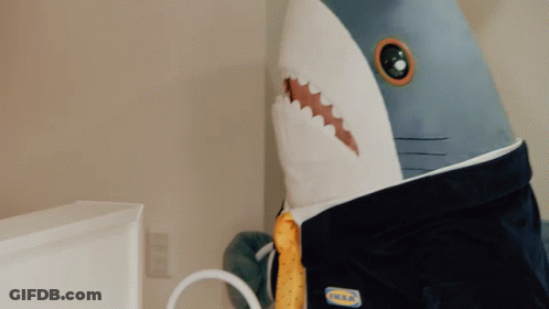 A Woman In A Yellow Shirt Holds A Stuffed Shark On Top Of A Bed GIF