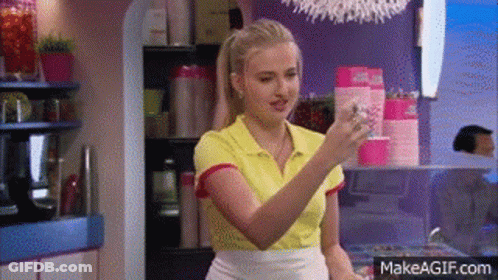 A Woman In A Yellow Shirt Is Holding A Glass Of Water In A Kitchen . GIF