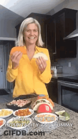 A Woman In A Yellow Shirt Is Holding A Taco In Her Hands And Smiling . GIF
