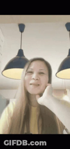 A Woman In A Yellow Shirt Is Making A Funny Face With Her Hand GIF