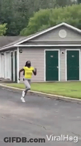 A Woman In A Yellow Shirt Is Running In Front Of A Building With Green Doors GIF