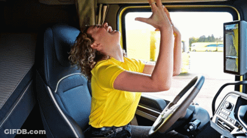 A Woman In A Yellow Shirt Is Sitting In The Driver 'S Seat Of A Semi Truck GIF