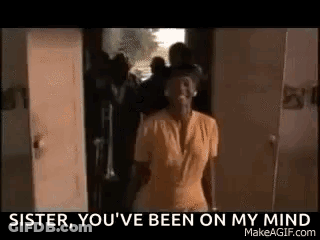 A Woman In A Yellow Shirt Is Standing In Front Of A Door And A Group Of Men . GIF
