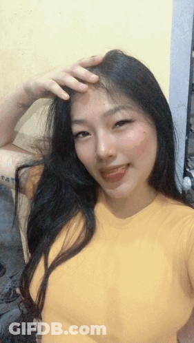 A Woman In A Yellow Shirt Is Taking A Selfie With Her Hand On Her Forehead GIF