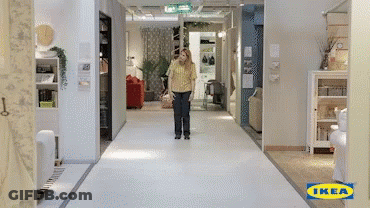 A Woman In A Yellow Shirt Is Walking Down A Hallway With An Ikea Logo On The Floor GIF