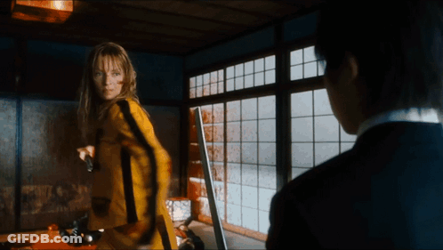 A Woman In A Yellow Suit Is Holding A Gun GIF