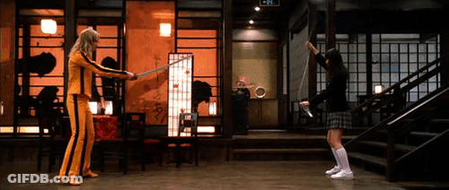 A Woman In A Yellow Suit Is Holding A Sword While Another Woman In A Black Skirt Holds A Sword GIF