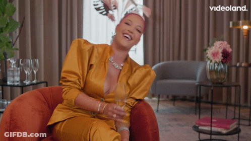 A Woman In A Yellow Suit Is Sitting In A Chair With A Videoland Logo In The Corner GIF